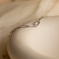 The Pave Link Chain Bracelet features delicate geometric links in silver, resting on a cream-colored surface—a minimalist and understated statement piece.