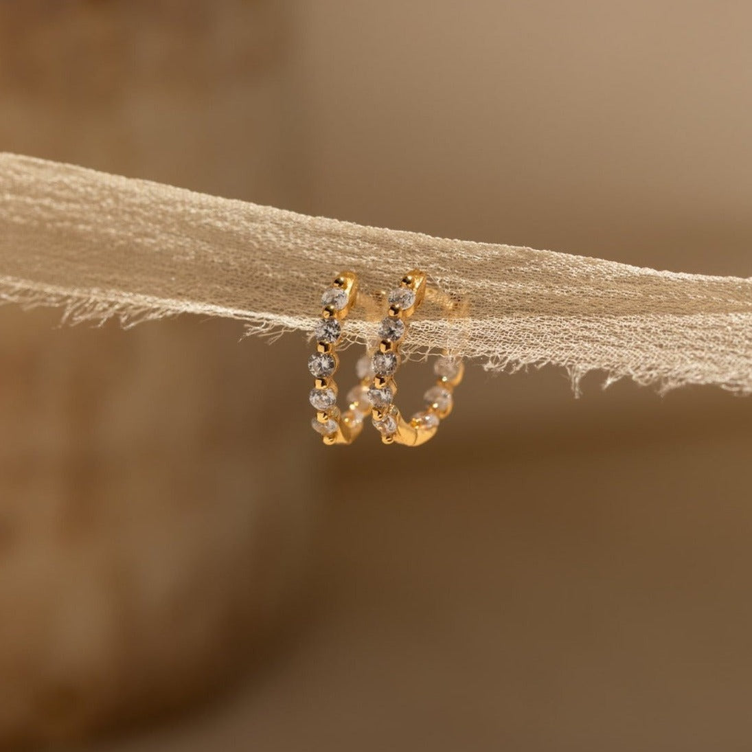 A pair of Inside Out Diamond Huggies with sparkling diamonds, displayed on a delicate textured beige fabric.