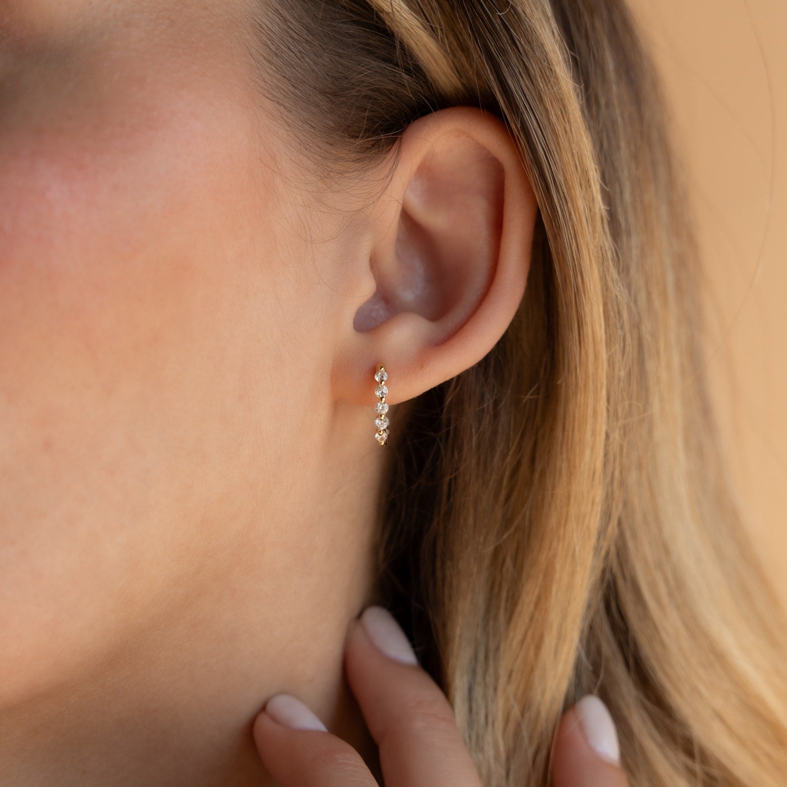 Close-up of a woman's ear wearing Inside Out Diamond Huggies in 18K Gold, featuring shimmering diamonds; her hand rests near her neck.