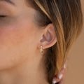 Close-up of a woman's ear wearing Inside Out Diamond Huggies—small gold hoops with five sparkling stones, hand gently near her neck.