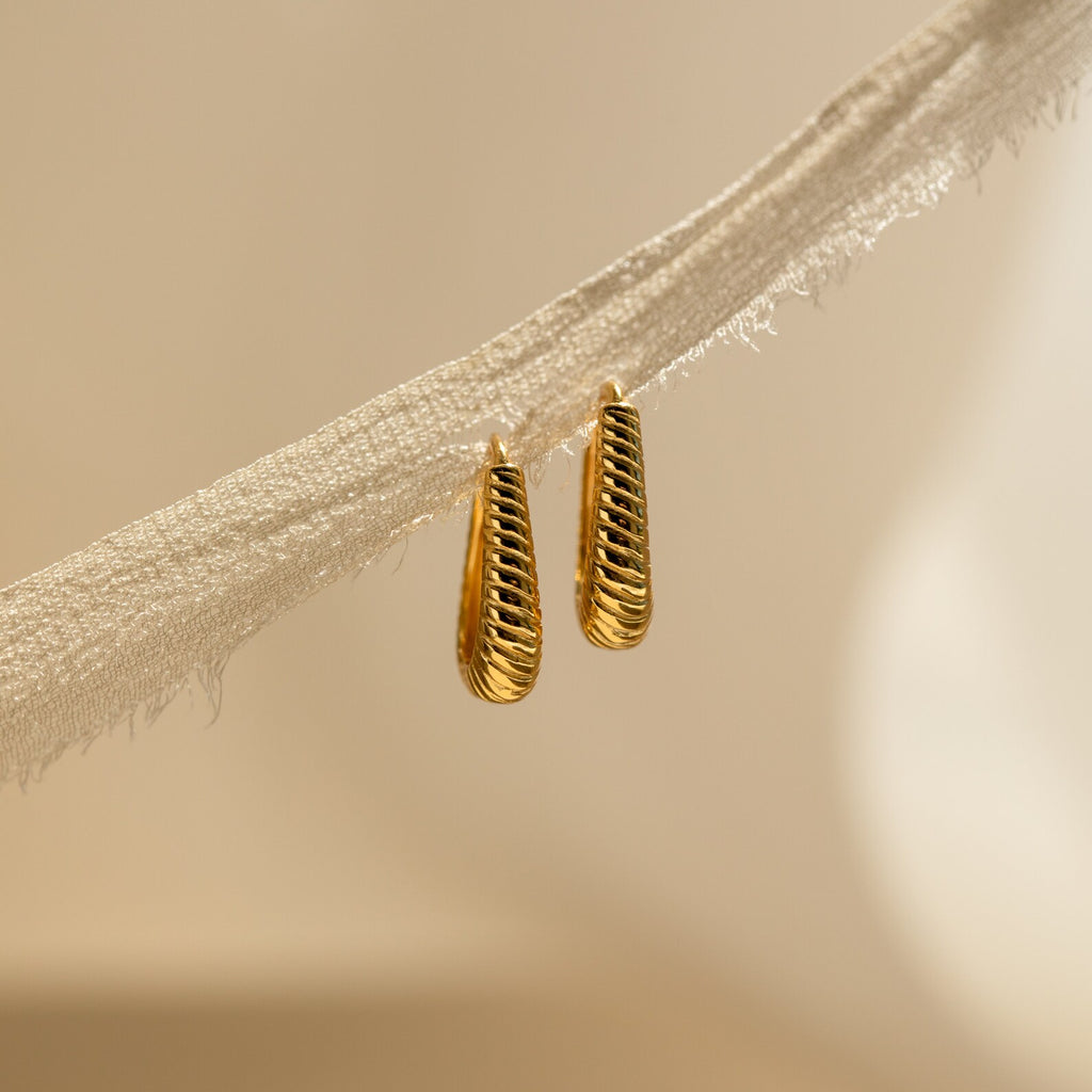Bold Ribbed Hoops with a textured, openwork geometric design hang on a piece of frayed, beige fabric.