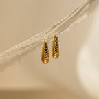 Bold Ribbed Hoops with a textured, openwork geometric design hang on a piece of frayed, beige fabric.