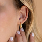 Close-up of a woman's ear wearing Bold Ribbed Hoops with fingers near her neck, showcasing the chic gold finish and subtle geometric ribbed design.