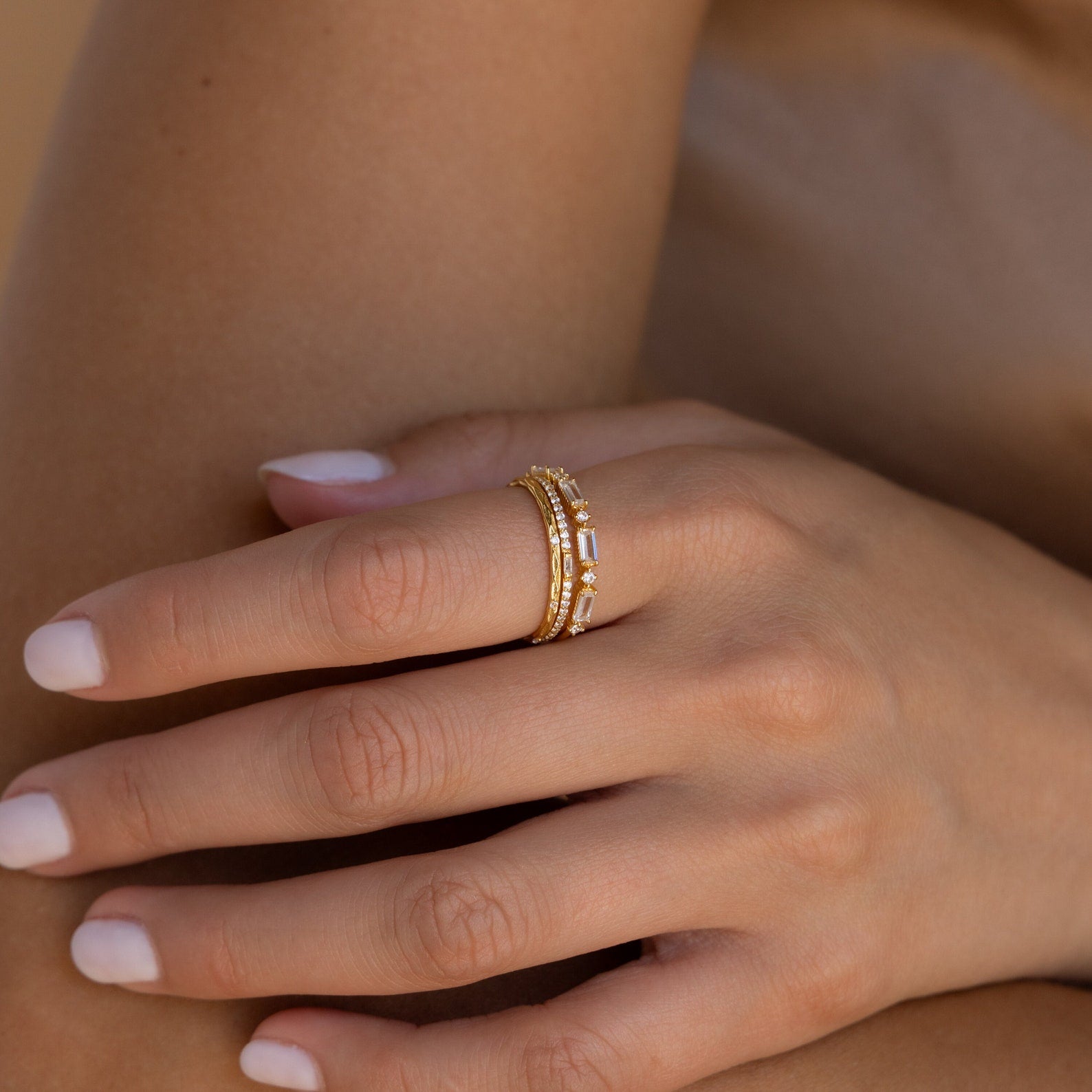 A hand with light pink nails wears several stacked gold rings, including the Diamond Stacking Ring Set in 18K Gold—a sparkling and elegant choice for a Christmas gift.