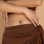 A woman’s midsection with crossed arms, wearing a brown wrap skirt and the Satellite Beaded Belly Chain in delicate gold.