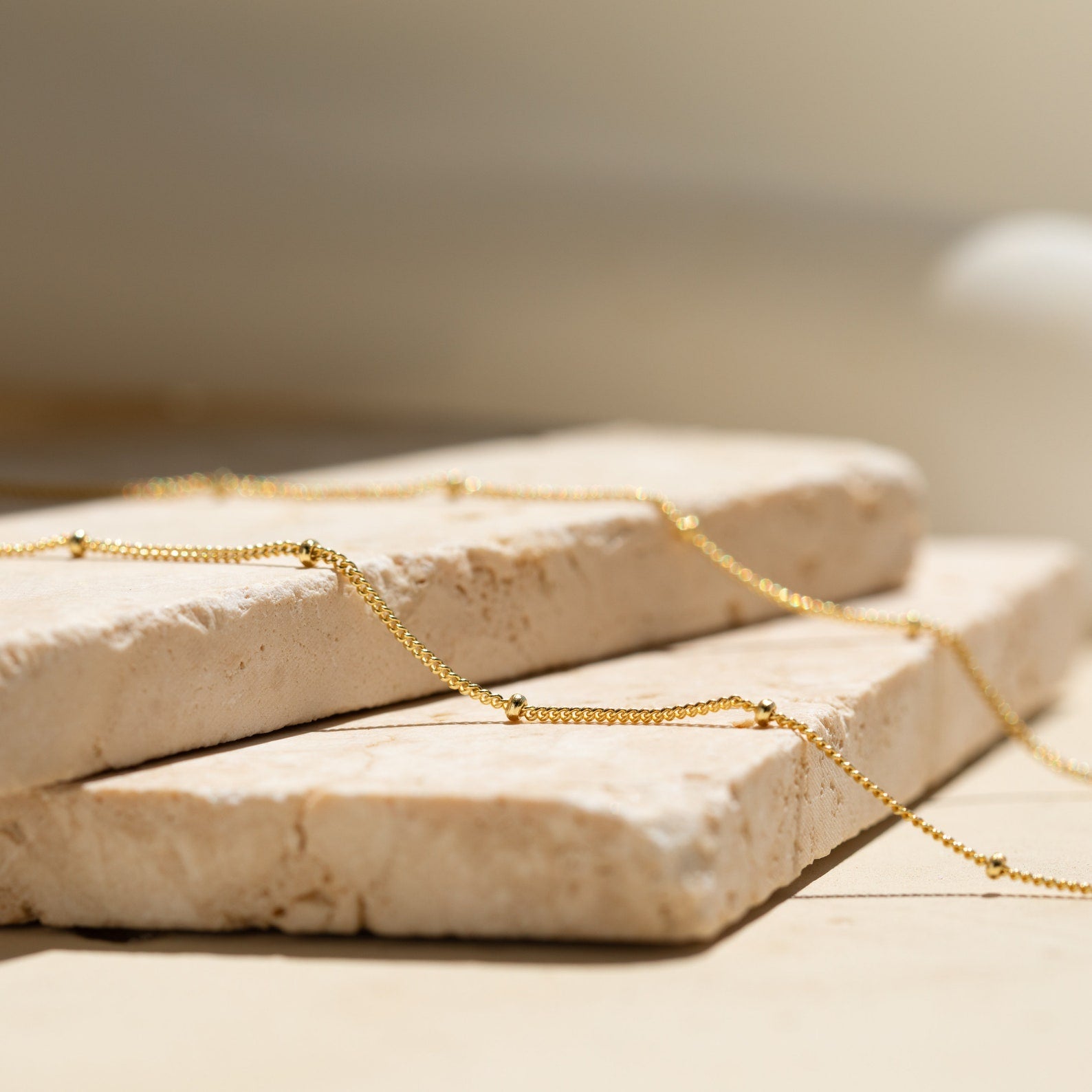 The Satellite Beaded Belly Chain, crafted in delicate gold, is showcased on two stacked beige stone slabs under soft natural light.