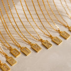 Gold initial pendant necklaces with rectangular charms featuring pavé crystal letters, displayed in a row on delicate chains over a soft fabric background.
