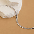 The Snake Chain Bracelet, ideal for minimalist stacks, is shown on white stone with a tan background.