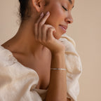 A woman with closed eyes gently touches her face, dressed in a cream blouse and wearing a delicate bracelet stack that highlights the sleek Snake Chain Bracelet.