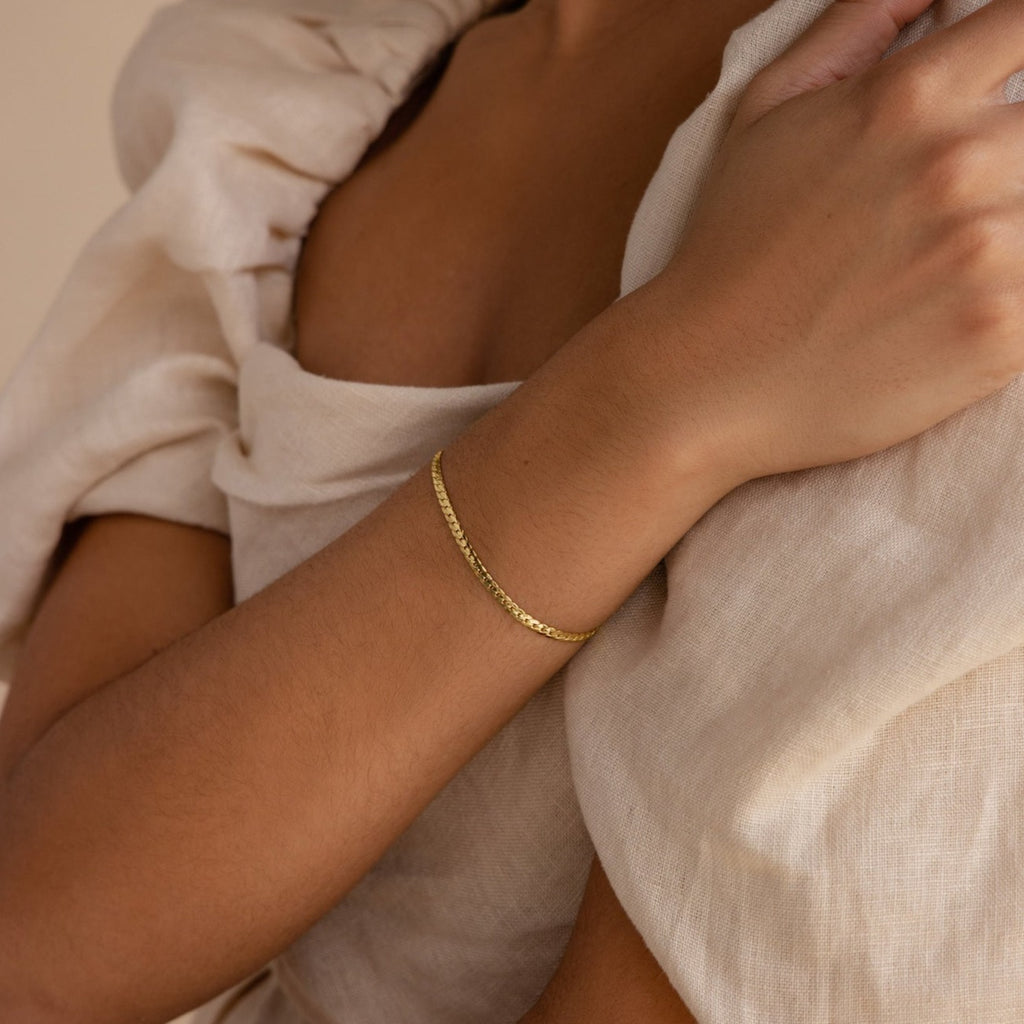 A person wearing a minimalist Snake Chain Bracelet and a beige, textured, off-the-shoulder top.