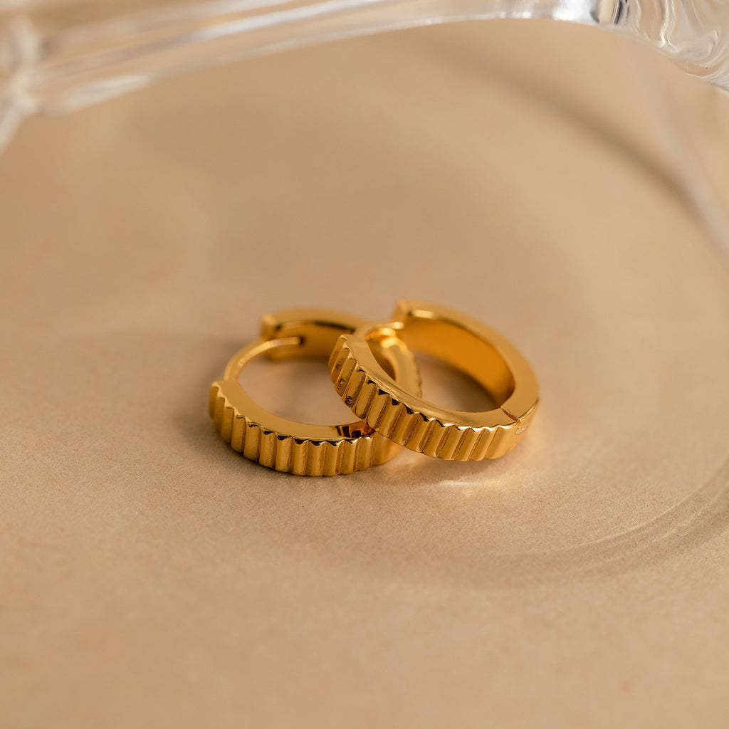 Ribbed Huggies displayed on a beige surface with a clear object in the background, offering the perfect balance of bold style and dainty elegance.