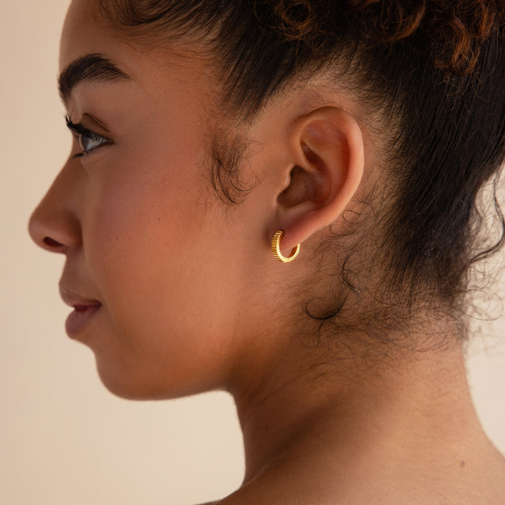 A woman in profile wears Ribbed Huggies, her curly hair pulled back to showcase the dainty earrings against a neutral background.