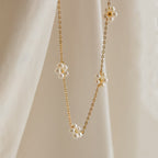 The Flower Pearl Station Necklace in 18K Gold features delicate flower-shaped pearl clusters, shown draped on soft beige fabric—a perfect bridesmaids gift or timeless accessory.