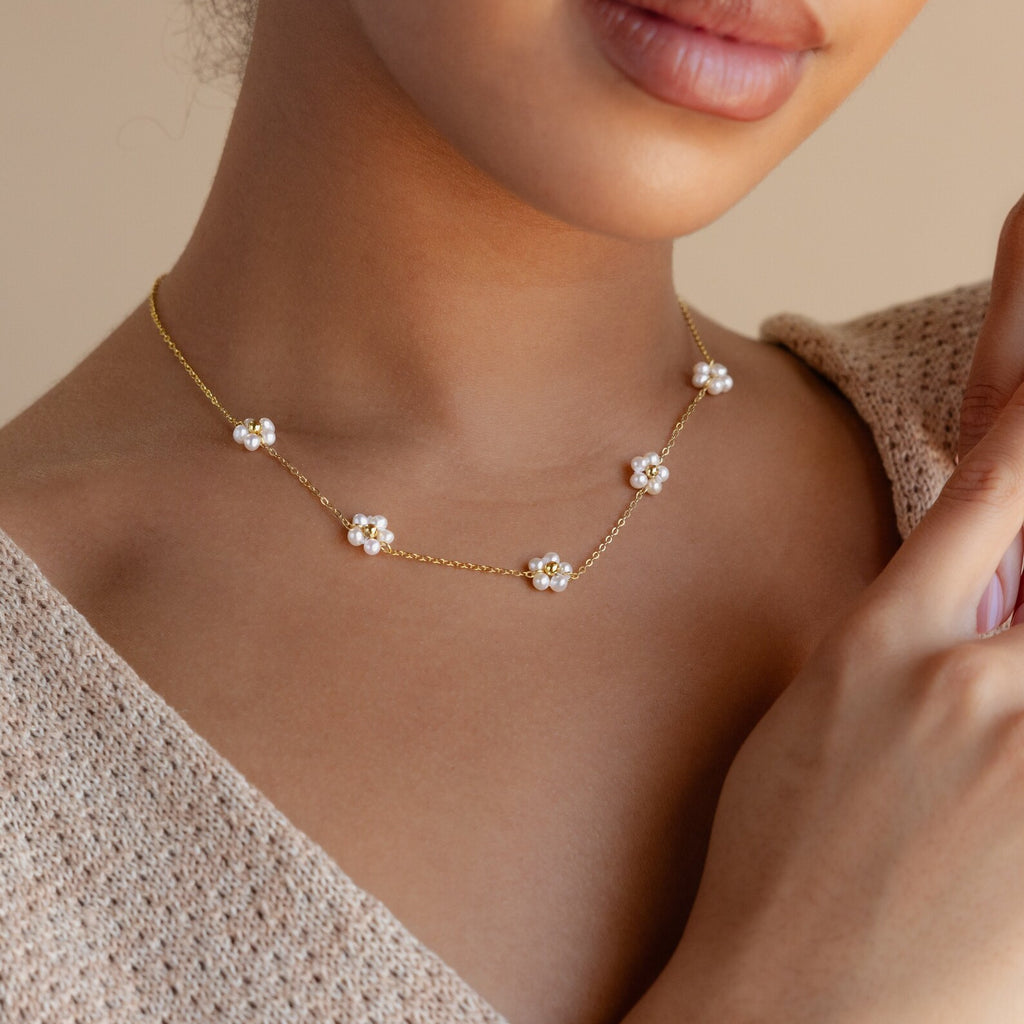 A woman wears the Flower Pearl Station Necklace, featuring delicate flower-shaped pendants, paired with a beige knit top—an elegant choice for a bridesmaid or Mother's Day gift.