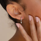 A close-up of a woman's ear adorned with elegant Opal Drop Huggies and her hand touching her face, nails painted light pink.