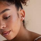 Woman with dewy skin wears gold Opal Drop Huggies, featuring elegant pearls, against a neutral background.