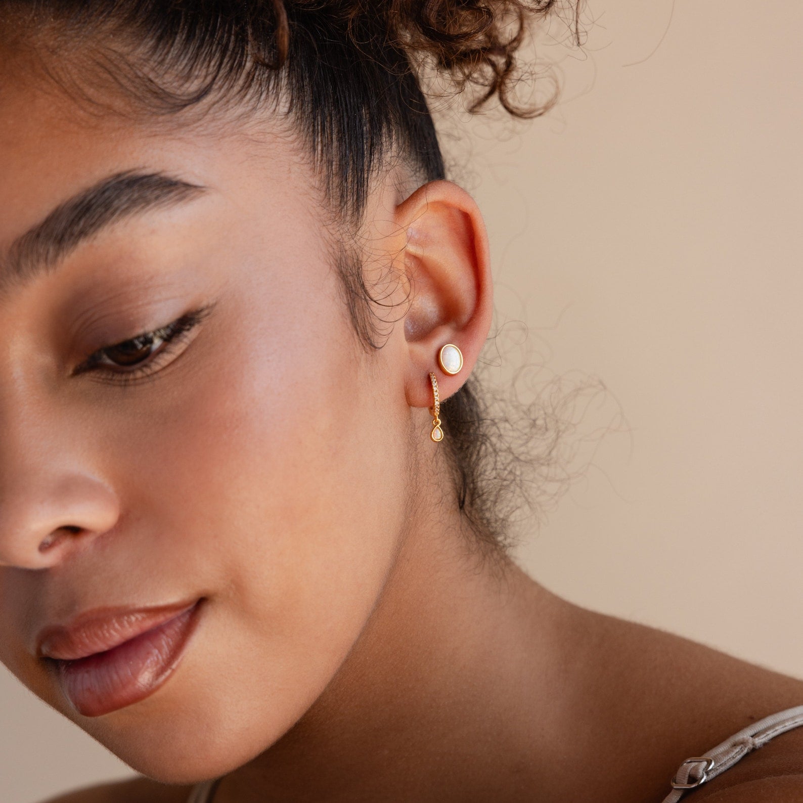 Woman with dewy skin wears gold Opal Drop Huggies, featuring elegant pearls, against a neutral background.