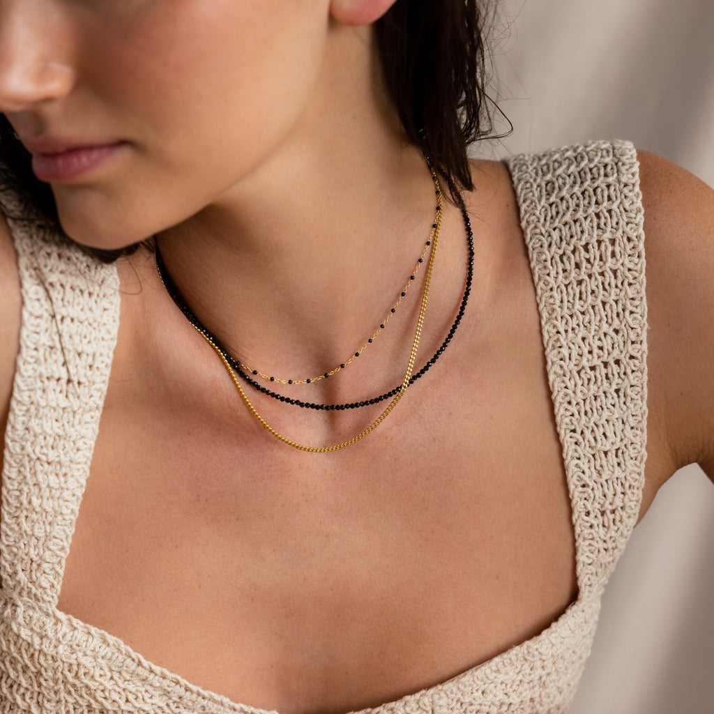 Woman wearing a crochet top and layering the Boho Beaded Necklaces—three bohemian strands with gold and black beads, perfect for breezy summer outfits.