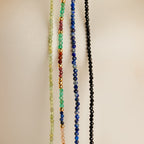 Five Boho Beaded Necklaces in green, blue, black, and multicolor hang vertically—ideal for layering and adding a playful vibe to your summer look.