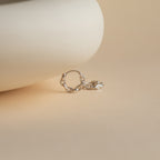 A single Link Huggies earring in silver rests on a smooth beige surface with a softly blurred background.