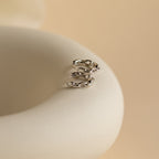 A pair of Link Huggies in silver rests on a white surface, perfect for adding subtle shine to your earring stack.