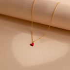 Gold chain necklace with a small red enamel heart pendant, displayed on a neutral background.
