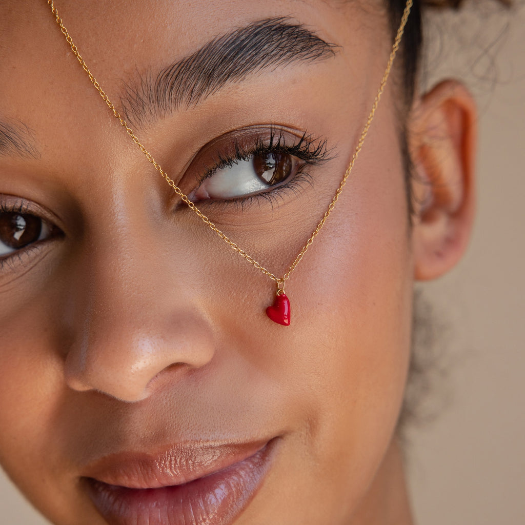 Close-up view of a woman wearing the Little Red Heart Necklace, a minimalist gold chain necklace featuring a red heart pendant.