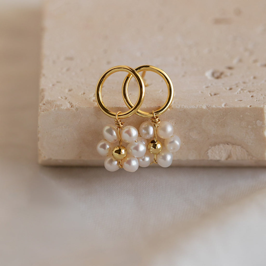 Flower Pearl Drop Earrings featuring gold hoops with delicate pearl flower clusters evoke a vintage feel, showcased on a beige textured surface.