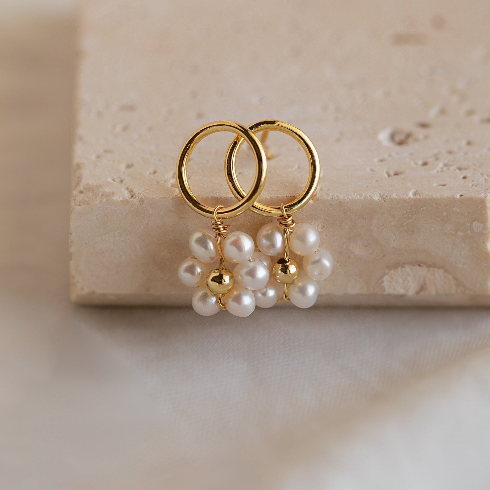 Flower Pearl Drop Earrings featuring gold hoops with delicate pearl flower clusters evoke a vintage feel, showcased on a beige textured surface.