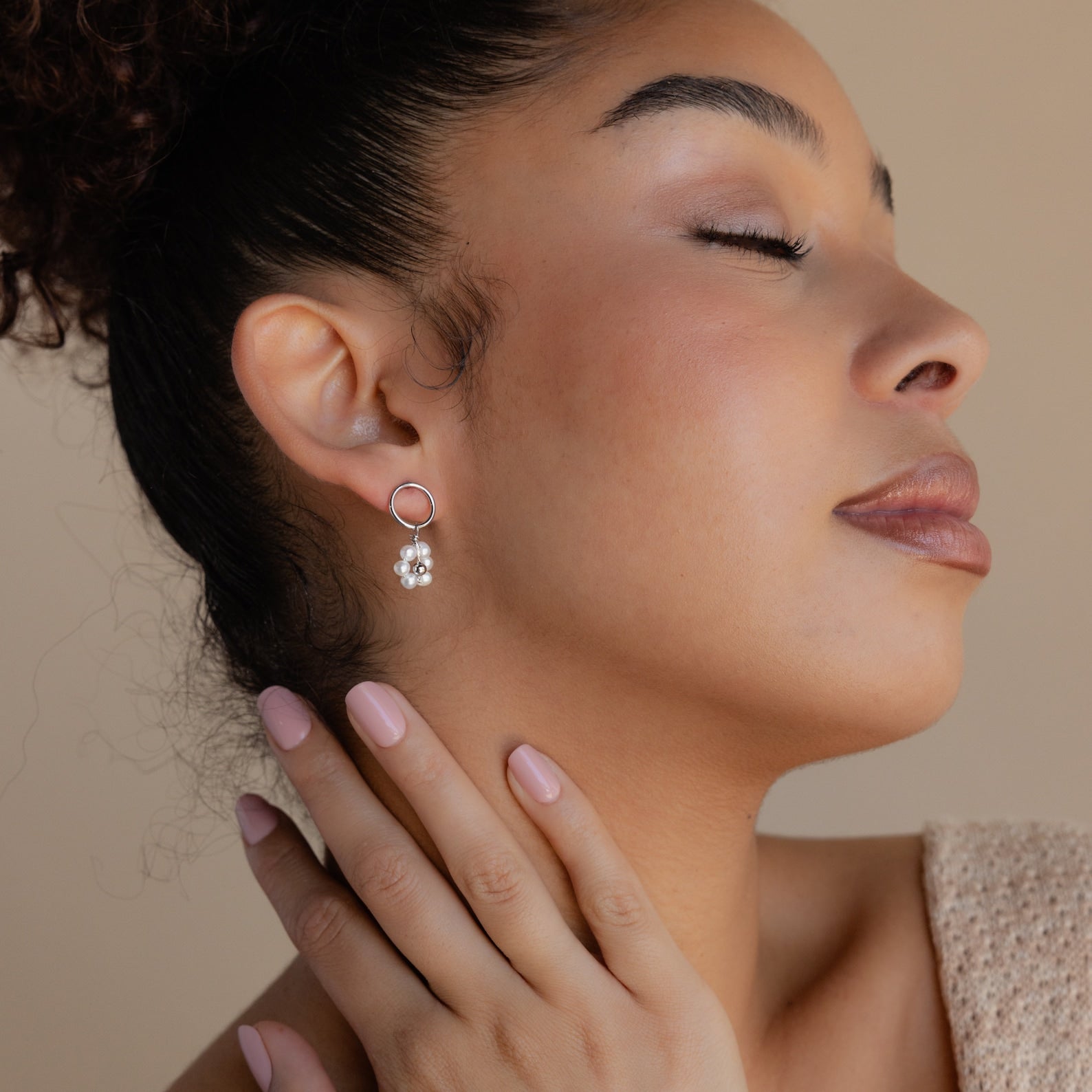 Woman with closed eyes gently touches her neck, showing off Flower Pearl Drop Earrings and soft pink nails.