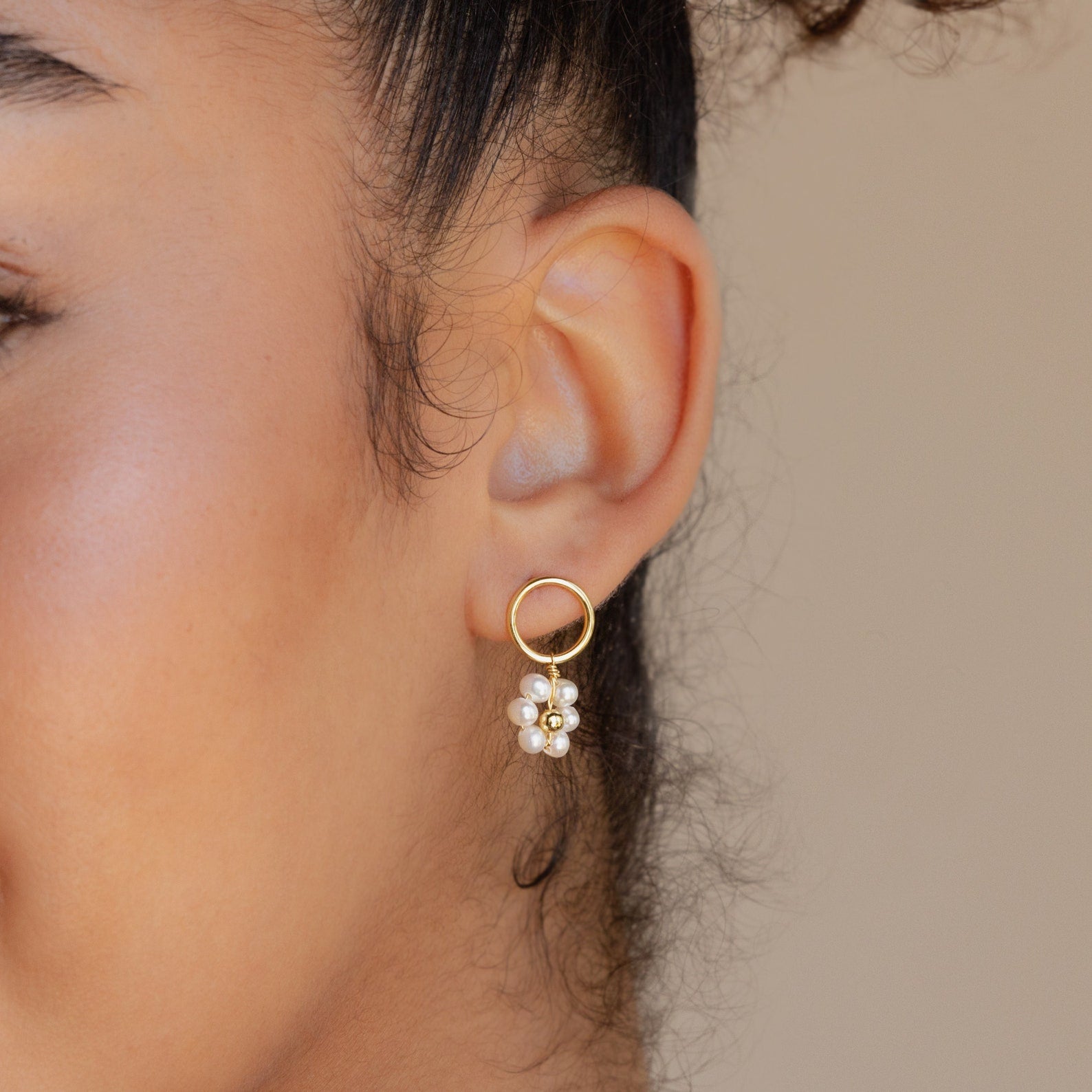Close-up of a woman's ear wearing Flower Pearl Drop Earrings—gold hoops adorned with dangling white pearl-like beads for a vintage-inspired look.