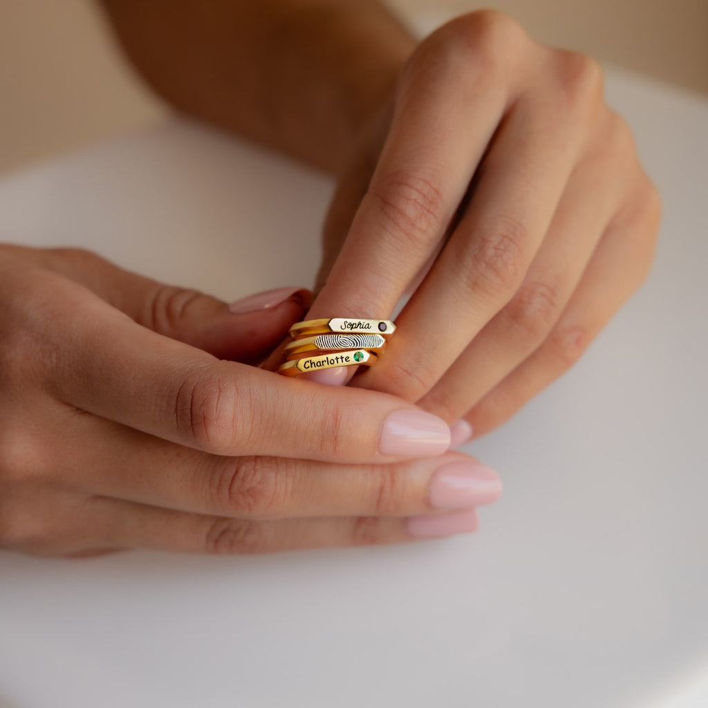 Close-up of hands holding a stacked Thin Fingerprint Signet Ring on a white surface—a unique personalized gift for any occasion.