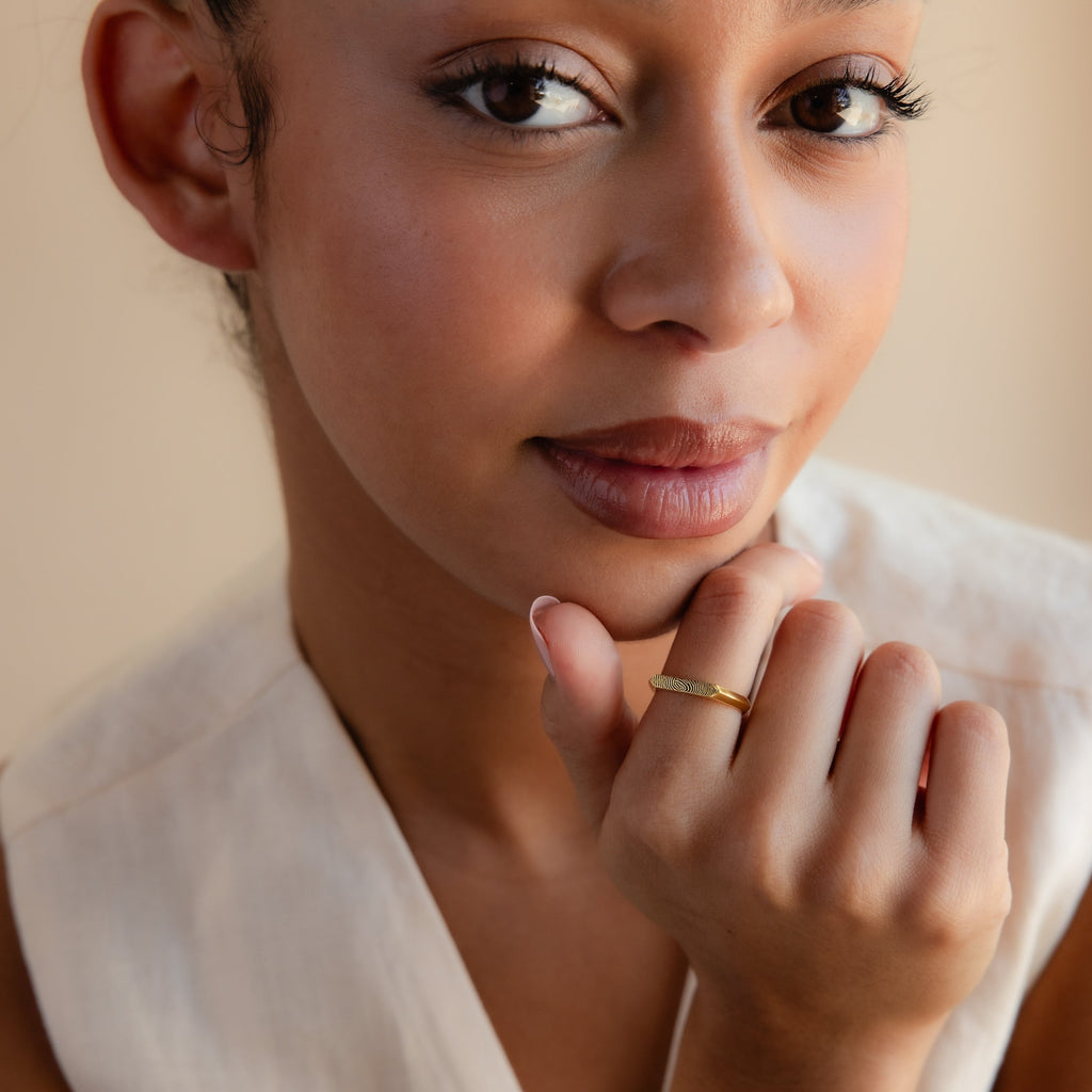 A woman with natural makeup in a sleeveless top showcases the Thin Fingerprint Signet Ring on her finger while gazing at the camera.