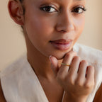 A woman with natural makeup in a sleeveless top showcases the Thin Fingerprint Signet Ring on her finger while gazing at the camera.