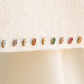 Nine pairs of Duo Birthstone Studs, featuring small colorful stones, are lined up on a cream fabric background—an ideal bridesmaids gift or a personalized touch for your everyday style.
