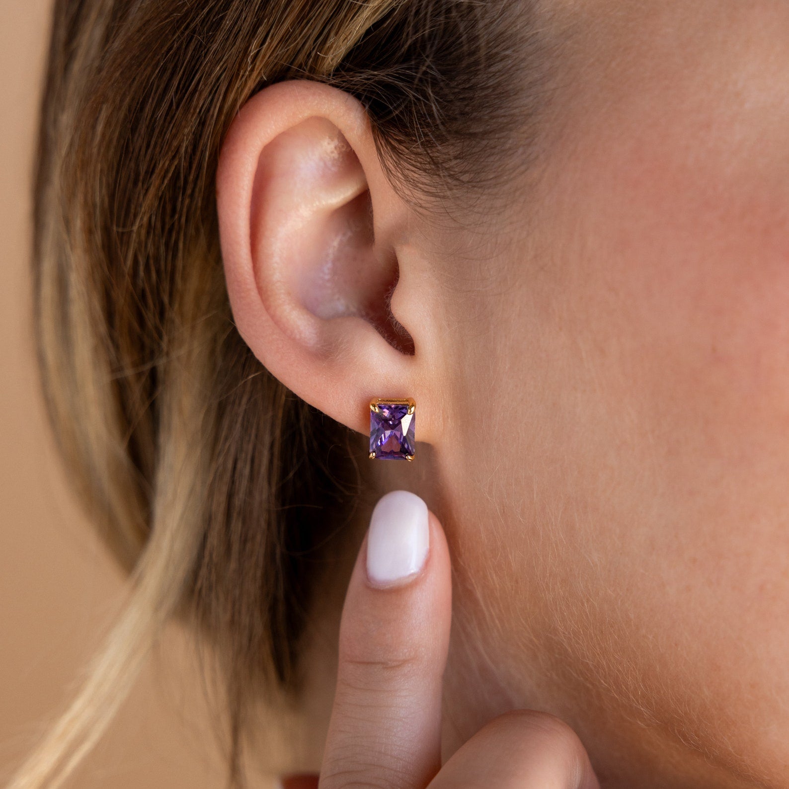 A hand points to an Emerald Birthstone Stud worn on a woman’s ear with light brown hair, making it an ideal personalized gift.