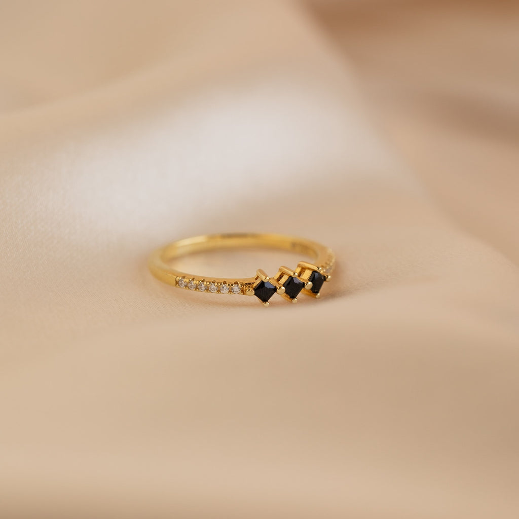 The Helena Black Diamond Ring features three black stones with small clear accents, shown on soft beige fabric—perfect for adding an edgy touch to your professional look.