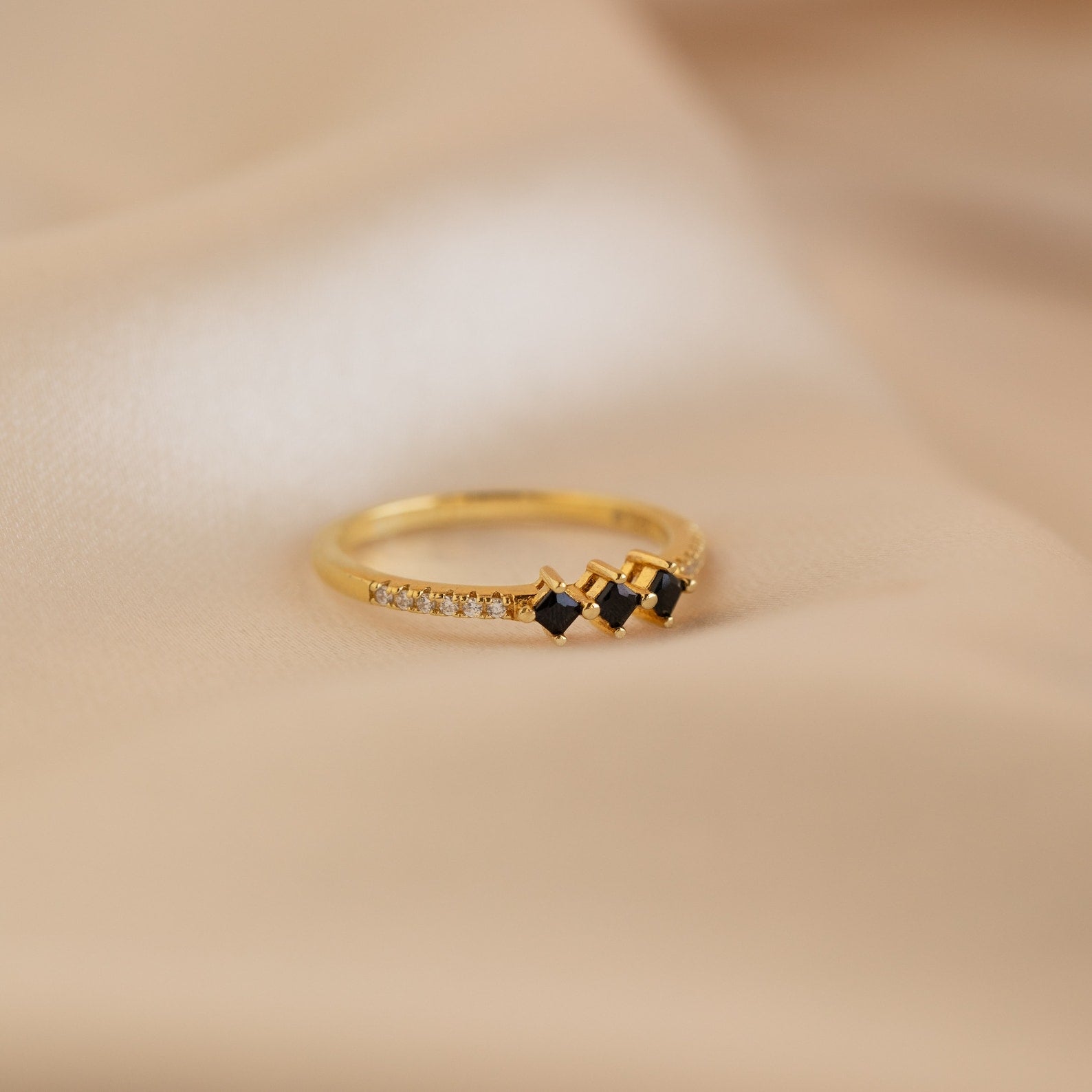 The Helena Black Diamond Ring features three black stones with small clear accents, shown on soft beige fabric—perfect for adding an edgy touch to your professional look.