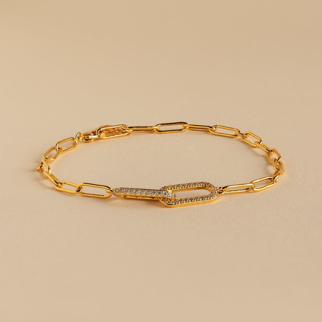 The Pave Link Chain Bracelet features elongated gold links and a crystal-encrusted clasp, making it an eye-catching statement piece, shown here on a beige background.