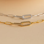 The Pave Link Chain Bracelet shines on a beige background, paired with gold and silver rectangular link chain necklaces—some accented with sparkling stones—for a bold, stylish look.