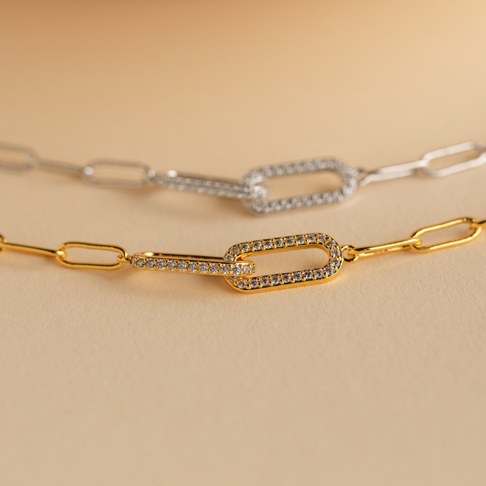 The Pave Link Chain Bracelet shines on a beige background, paired with gold and silver rectangular link chain necklaces—some accented with sparkling stones—for a bold, stylish look.
