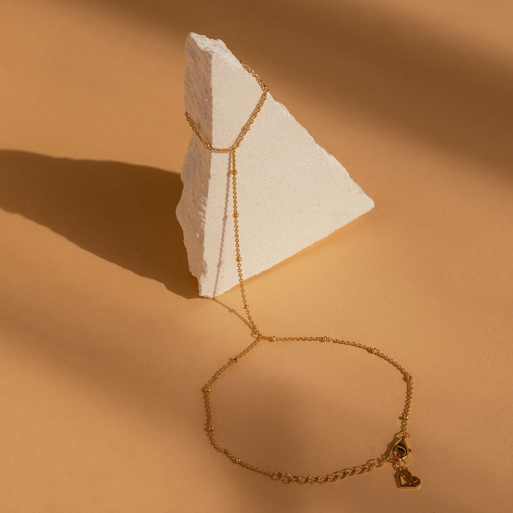 Beaded Hand Chain Bracelet elegantly displayed on a white triangular stone against a beige background—a chic statement piece that enhances any outfit.