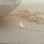 The Newsletter Initial Bracelet rests on a light, textured surface—perfect for pairing with a delicate necklace or personalized jewelry for a truly unique touch.