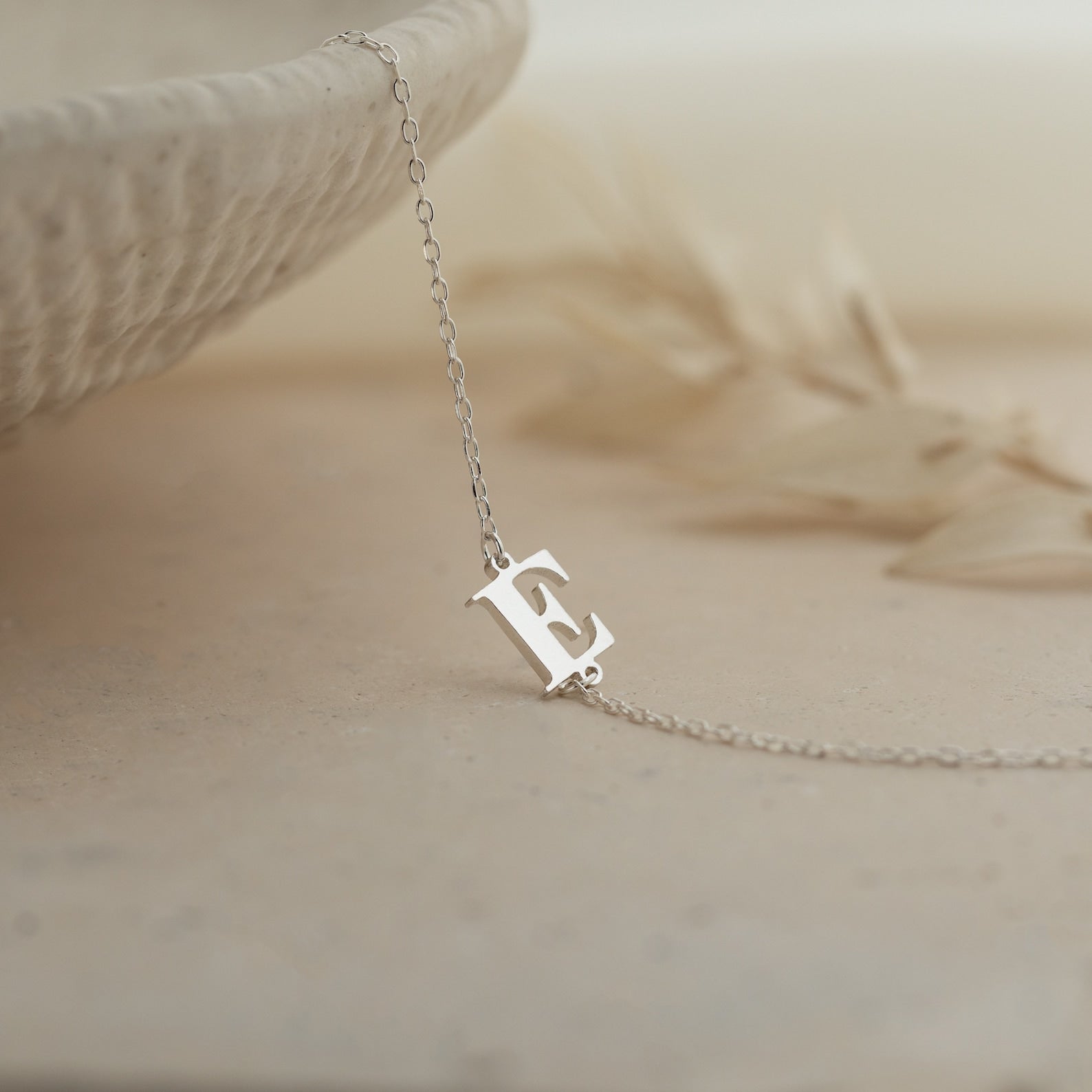 The Newsletter Initial Bracelet rests on a light, textured surface—perfect for pairing with a delicate necklace or personalized jewelry for a truly unique touch.