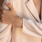 A person wearing a beige blazer and the Newsletter Initial Bracelet—a delicate, personalized bracelet with an E charm.