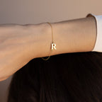 The Newsletter Initial Bracelet, featuring a gold letter R charm, elegantly adorns the wrist against a neutral background—making it a stylish personalized accessory for any occasion.