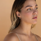 Woman with long hair wearing a thin strap top and Pave Sun Huggies, gazing slightly upward against a beige background.