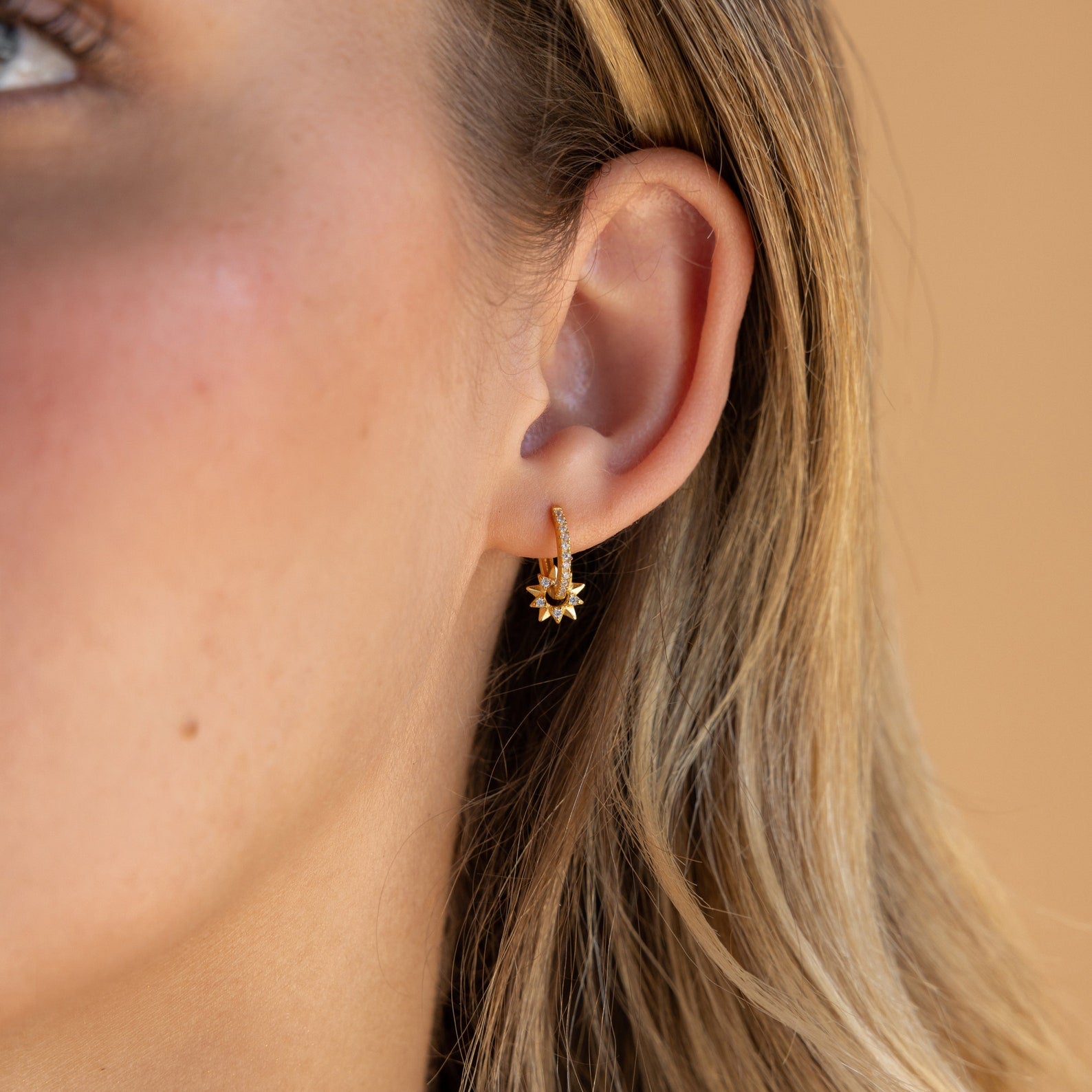 Close-up of a woman's ear wearing Pave Sun Huggies, featuring a small gold hoop adorned with a sparkling sun-shaped charm.