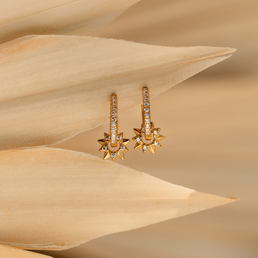 The Pave Sun Huggies are gold diamond earrings featuring sparkling stones on a delicate leaf, perfect for adding elegance to your look.