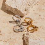 Two pairs of Pave Sun Huggies, one gold and one silver, displayed on light textured stone—a celestial twist on classic hoops.